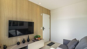 Ein modernes Wohnzimmer mit einem an einer Holzwand montierten Flachbildfernseher, einem grauen Sofa und einem kleinen Konsolentisch mit Dekoration.