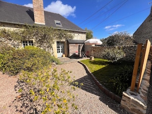 A stone house with a gravel driveway, a small garden, and a wooden deck.