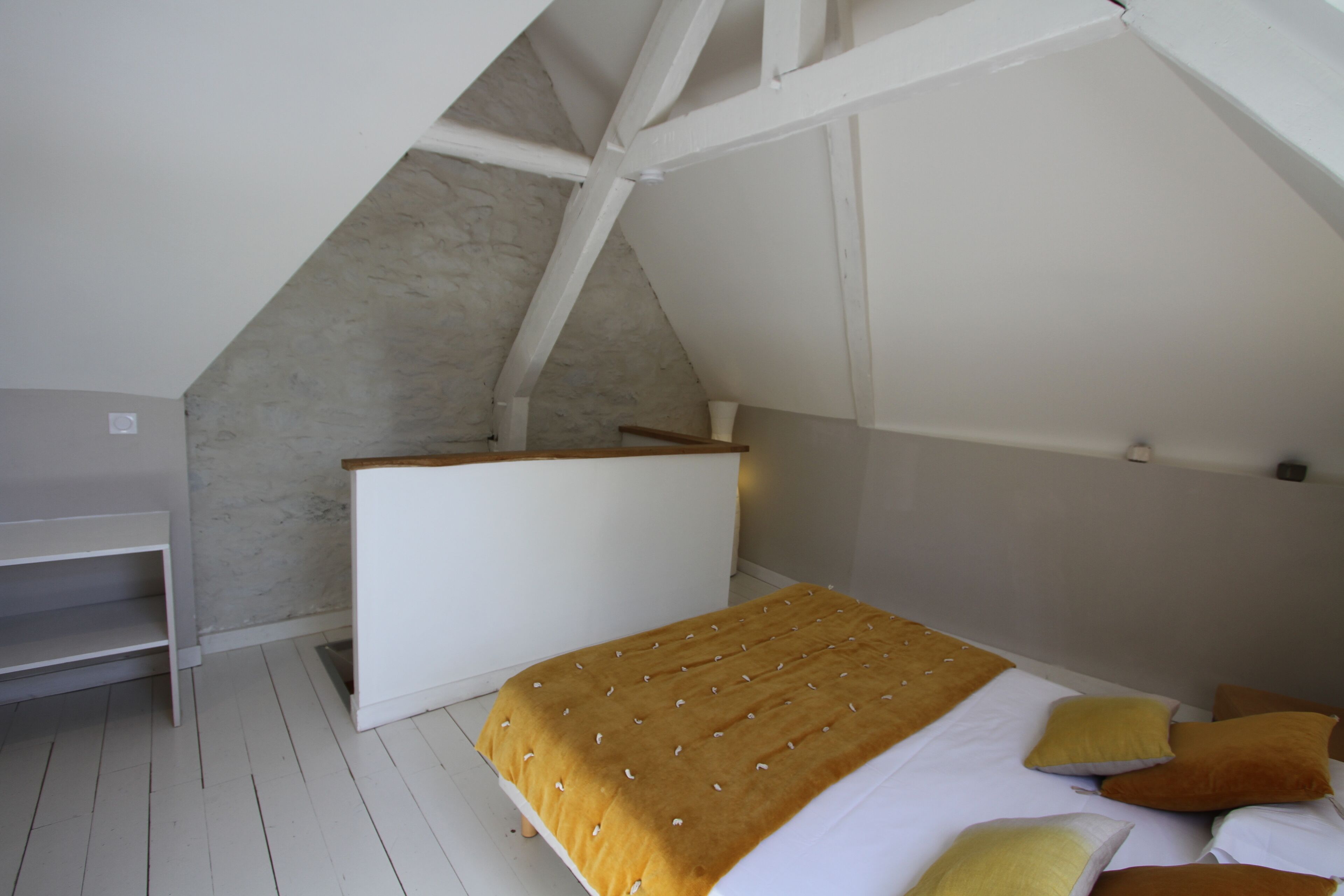 A bedroom with a sloped ceiling, a bed with a patterned bedspread, and a white wardrobe.