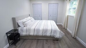 A bedroom with a bed, a nightstand, two closets, and a window with curtains.
