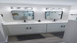 A modern bathroom with two sinks, a large mirror, and a lighted vanity.