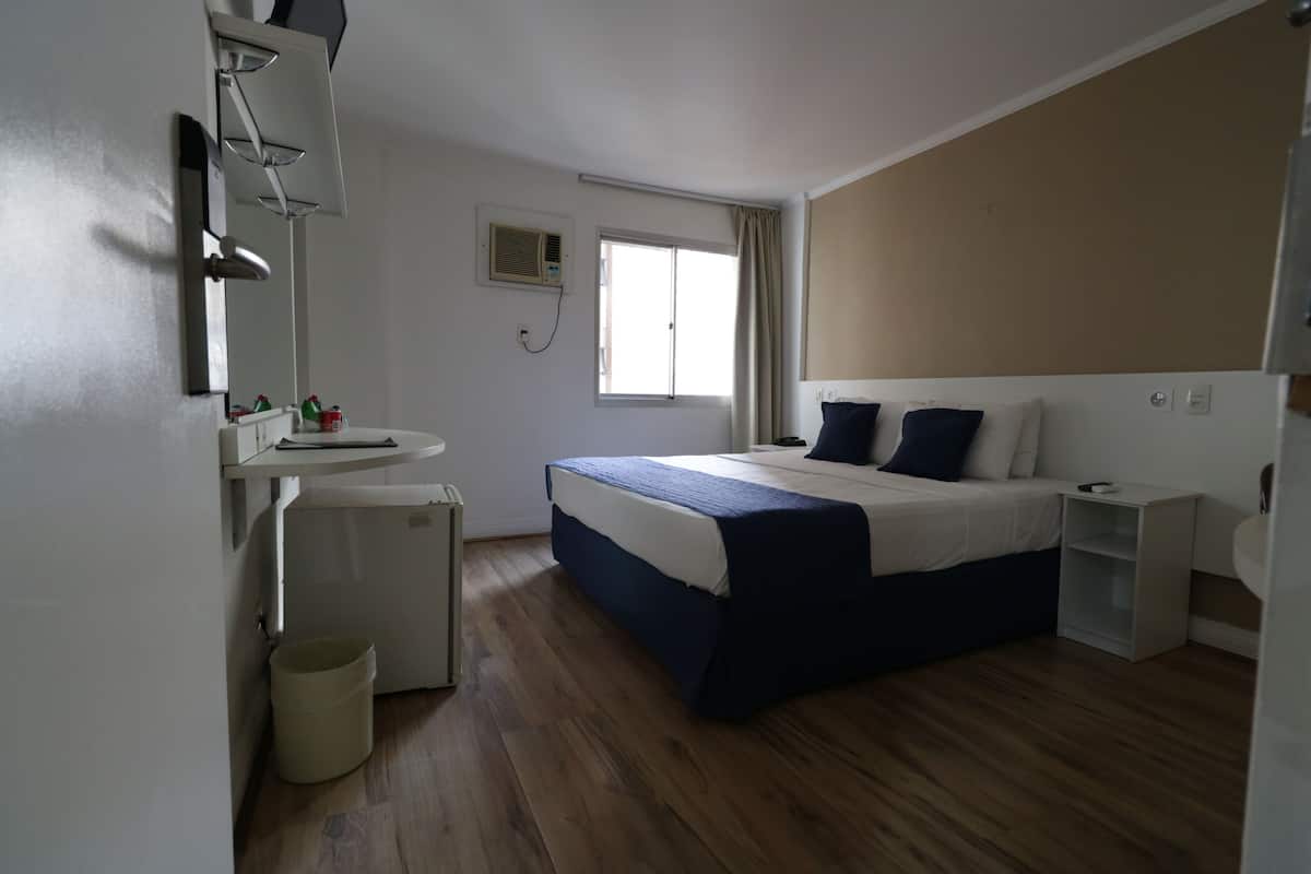 Une chambre à coucher avec un lit, une table de chevet, un petit bureau, une fenêtre et un miroir.