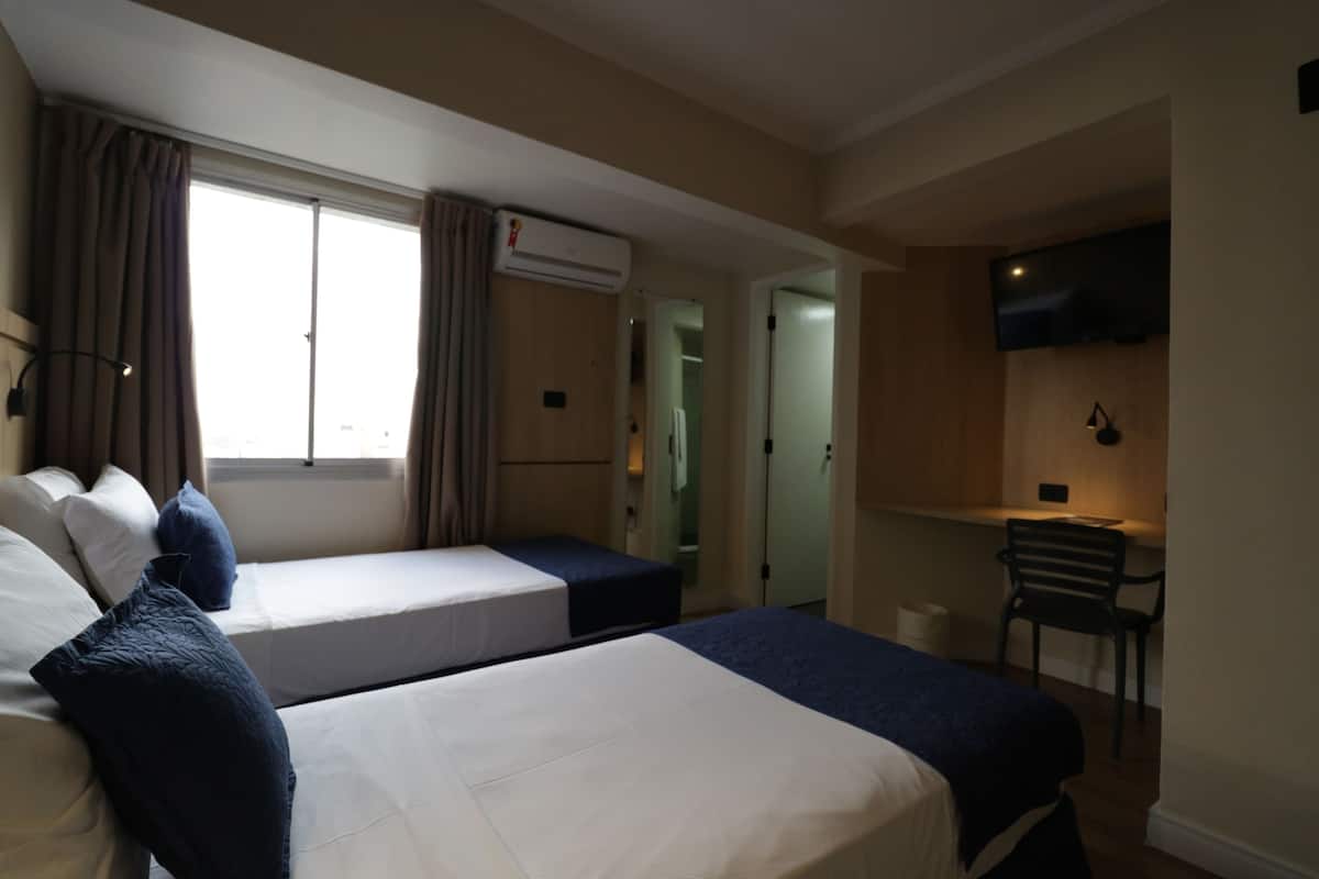 Une chambre d’hôtel avec deux lits, un bureau, une chaise, une télévision et un appareil de climatisation.