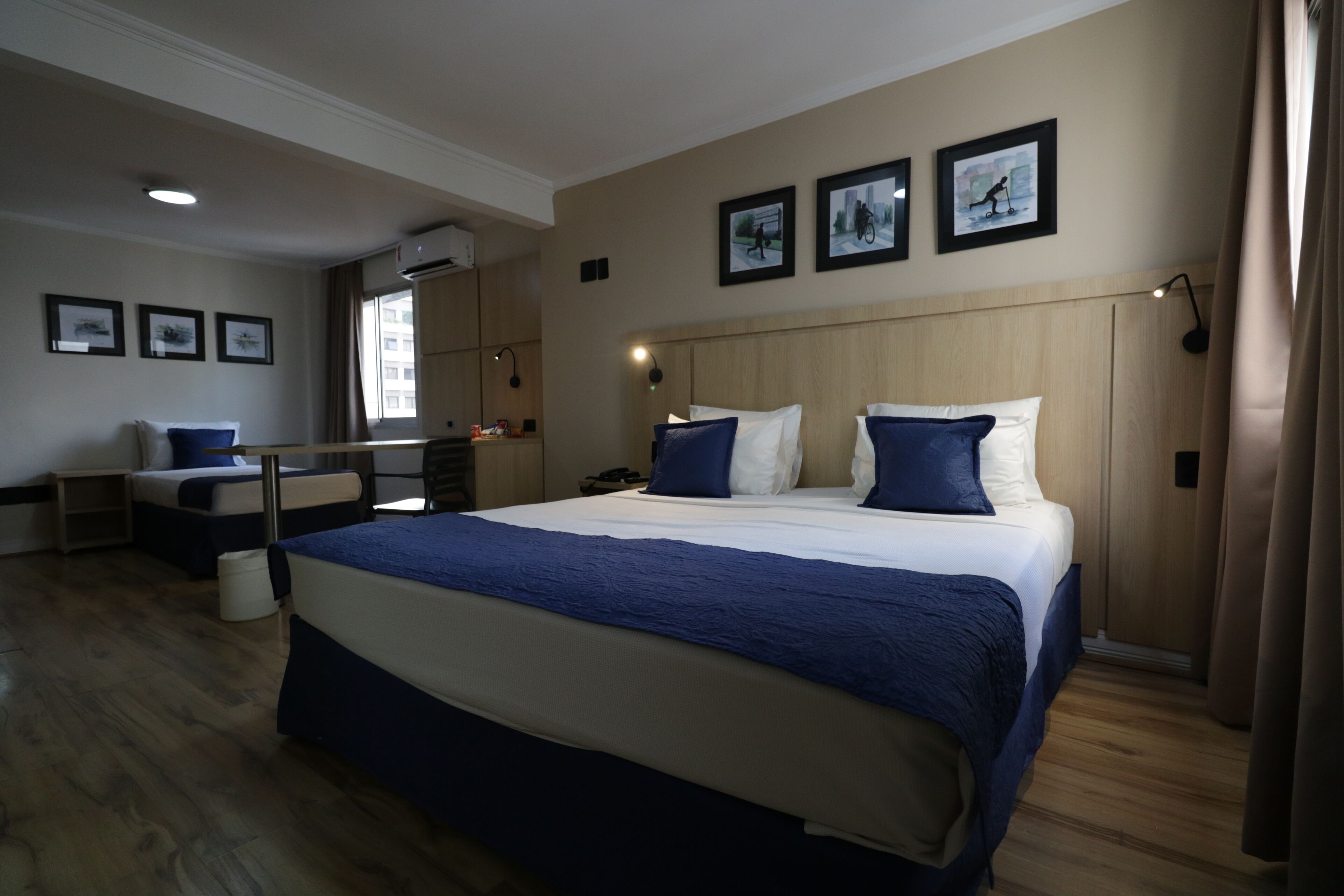 A modern hotel room with a large bed, a desk, and a chair. There are three framed pictures on the wall.