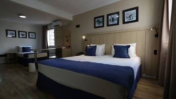 A modern hotel room with a large bed, a desk, and a chair. There are three framed pictures on the wall.