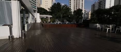 A rooftop deck with wooden flooring, lounge chairs, and a pool area.