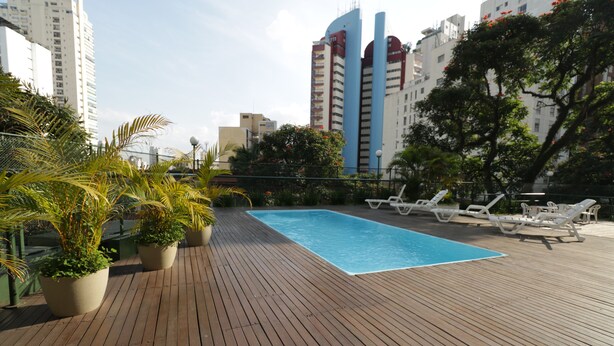 A rooftop pool area with wooden decking, lounge chairs, and potted plants.
