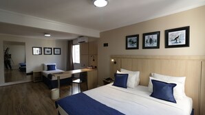 A hotel room with a large bed, a desk, and a mirror. There are framed pictures on the wall and a ceiling light.