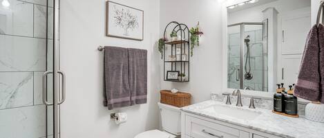 Un baño moderno con cabina de ducha de vidrio, inodoro, tocador con espejo y barra para toallas.