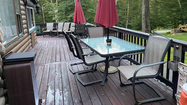 A wooden deck with outdoor furniture, including a table and chairs, and two red umbrellas. - Soothing cabin at Great sacandaga lake come enjoy the peace in a rural area. (Hadley)