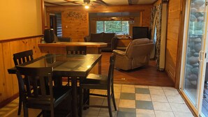 A wooden interior with a dining table, chairs, a sofa, and a television. - Soothing cabin at Great sacandaga lake come enjoy the peace in a rural area. (Hadley)