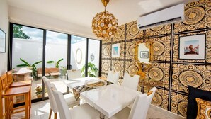 A dining area with a glass table, white chairs, and a patterned wall. - Charming & Comfortable House, 15 min to Downtown (Playa del Carmen)