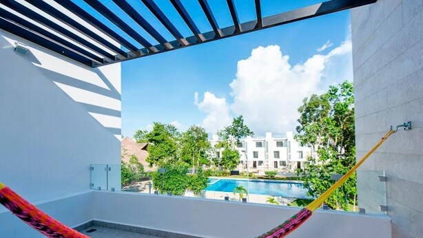 A balcony with a hammock, a pool, and a view of a residential area. - Charming & Comfortable House, 15 min to Downtown (Playa del Carmen)