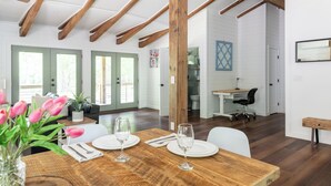 Un comedor amplio con una mesa de madera dispuesta para cuatro, una cocina al fondo y vistas al exterior a través de grandes ventanales.