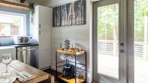 Una cocina con una mesa de madera, una cafetera y un microondas. Hay una puerta corrediza de vidrio que da a una terraza al aire libre.