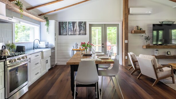 Una cocina moderna con una mesa de madera, sillas blancas y una zona de comedor con televisión y asientos.