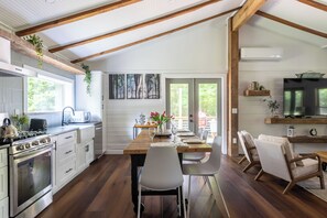Una cocina moderna con una mesa de madera, sillas blancas y una zona de comedor con televisión y asientos.