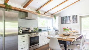 Una cocina moderna con electrodomésticos de acero inoxidable, armarios blancos y una mesa de comedor de madera preparada para seis personas.