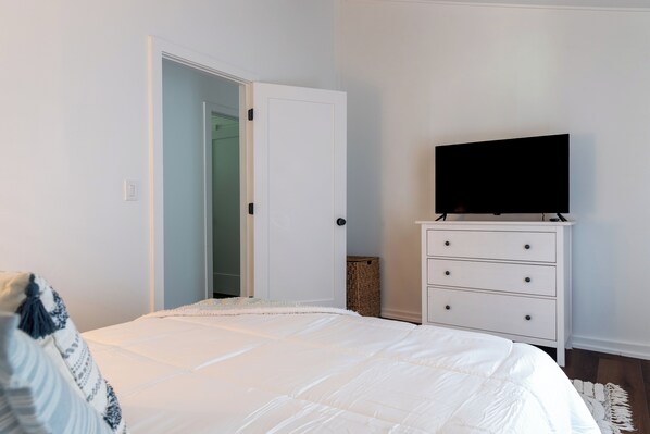 Un dormitorio con una cama, un aparador, un televisor y una puerta que da a otra habitación.