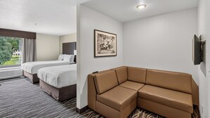Une chambre d’hôtel avec deux lits, un canapé marron, un tableau encadré au mur et une fenêtre avec des rideaux.