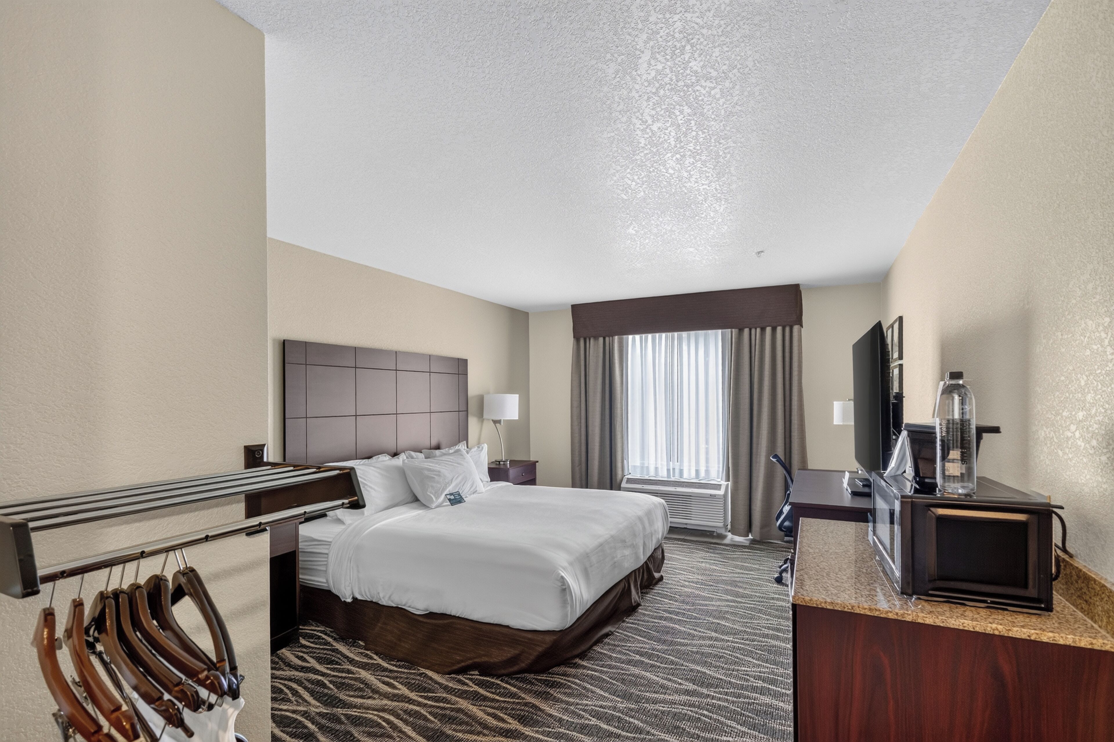 A hotel room with a bed, a desk, a television, and a window with curtains.