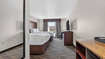 A hotel room with two beds, a desk, a TV, and a view of the outside.