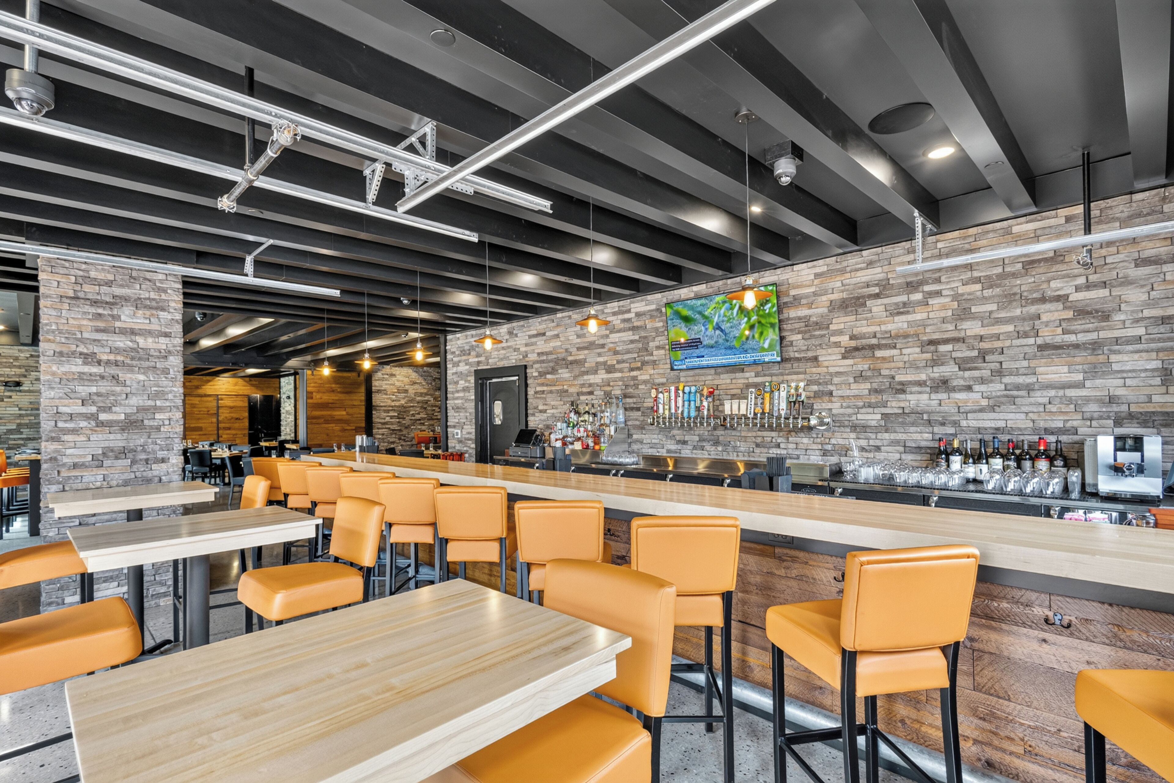 A bar area with a brick wall, bar stools, and a counter with bottles.