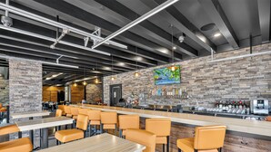 Un espace bar avec un mur en briques, des tabourets de bar et un comptoir où sont exposées des bouteilles.