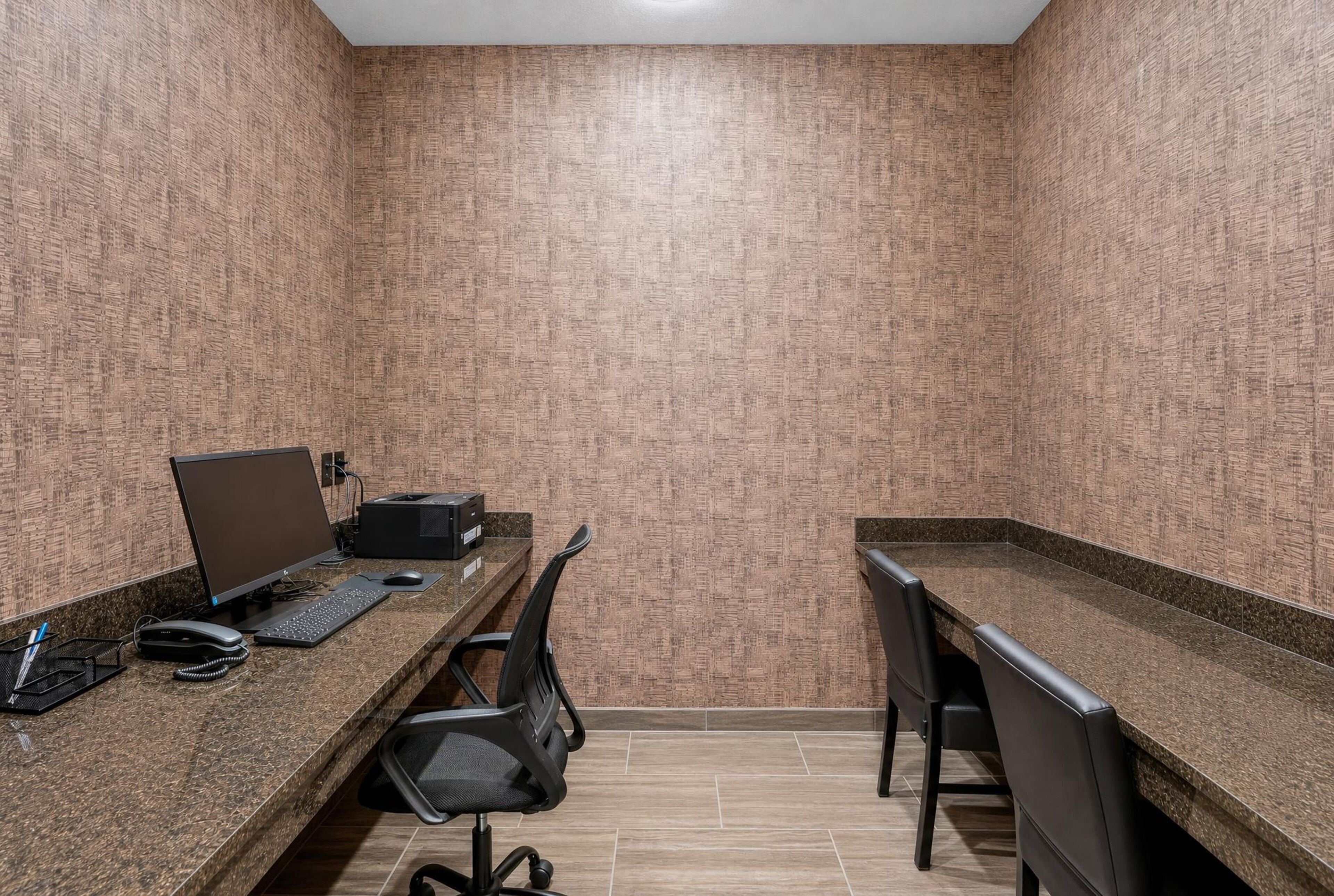 A small, enclosed office space with two desks, one with a computer and keyboard, and the other with a printer. There are chairs and a telephone on the desks.