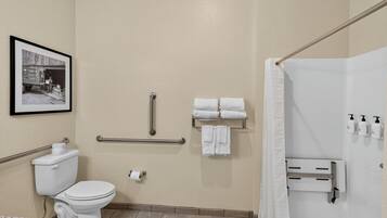 A bathroom with a toilet, a handrail, a towel rack, and a shower area.