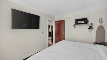 A hotel room with a bed, a mounted television, a coat rack, and a door leading to a bathroom.