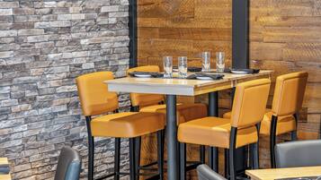 A restaurant interior with a stone wall, wooden panel wall, and yellow chairs around a table with glasses and cutlery.