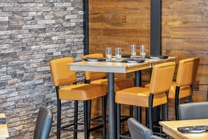 Interior de restaurante con pared de piedra, panel de madera y sillas amarillas alrededor de una mesa con vasos y cubiertos.