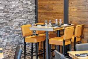 Interior de restaurante con pared de piedra, panel de madera y sillas amarillas alrededor de una mesa con vasos y cubiertos.