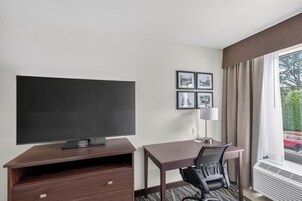 Habitación de hotel con televisión de pantalla plana, escritorio, silla, lámpara y ventana con cortinas.