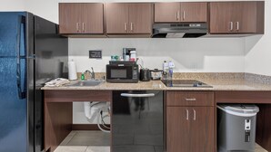A modern kitchen with wooden cabinets, a stainless steel refrigerator, a microwave, and a dishwasher. - Cobblestone Hotel & Suites - Waukesha/West Milwaukee (Waukesha)