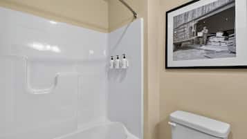 A bathroom with a white bathtub, a toilet, and a framed black and white photograph on the wall.
