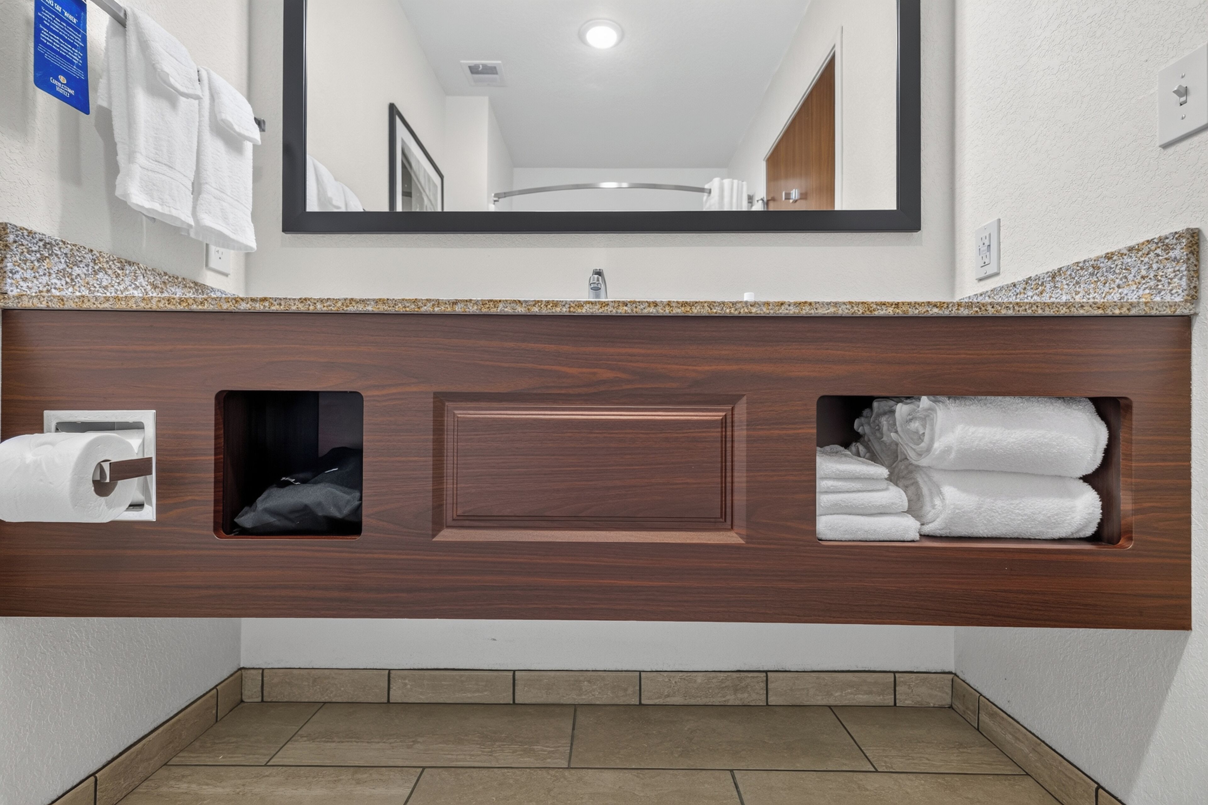 Een badkamer met een houten wastafelmeubel, een spiegel, een handdoekrek en een toiletrolhouder.