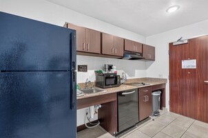 Una cocina compacta con refrigerador, microondas, lavaplatos y alacenas.