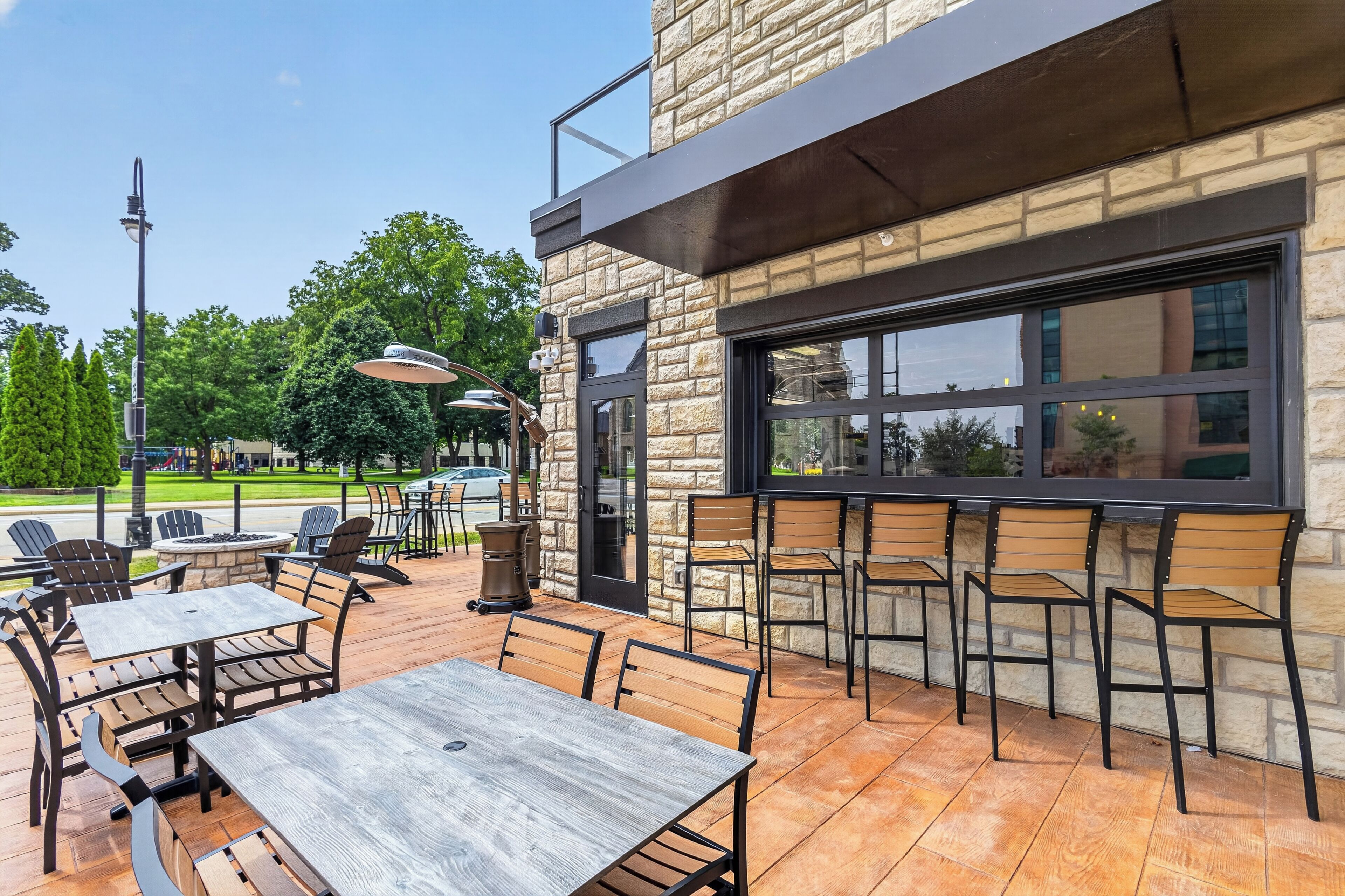 An outdoor seating area with tables and chairs, a stone building with a large window, and a clear sky.