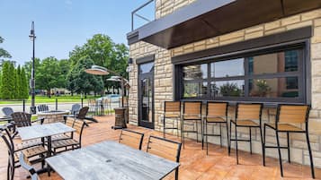 An outdoor seating area with tables and chairs, a stone building with a large window, and a clear sky.