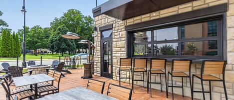 An outdoor seating area with tables and chairs, a stone building with a large window, and a clear sky.