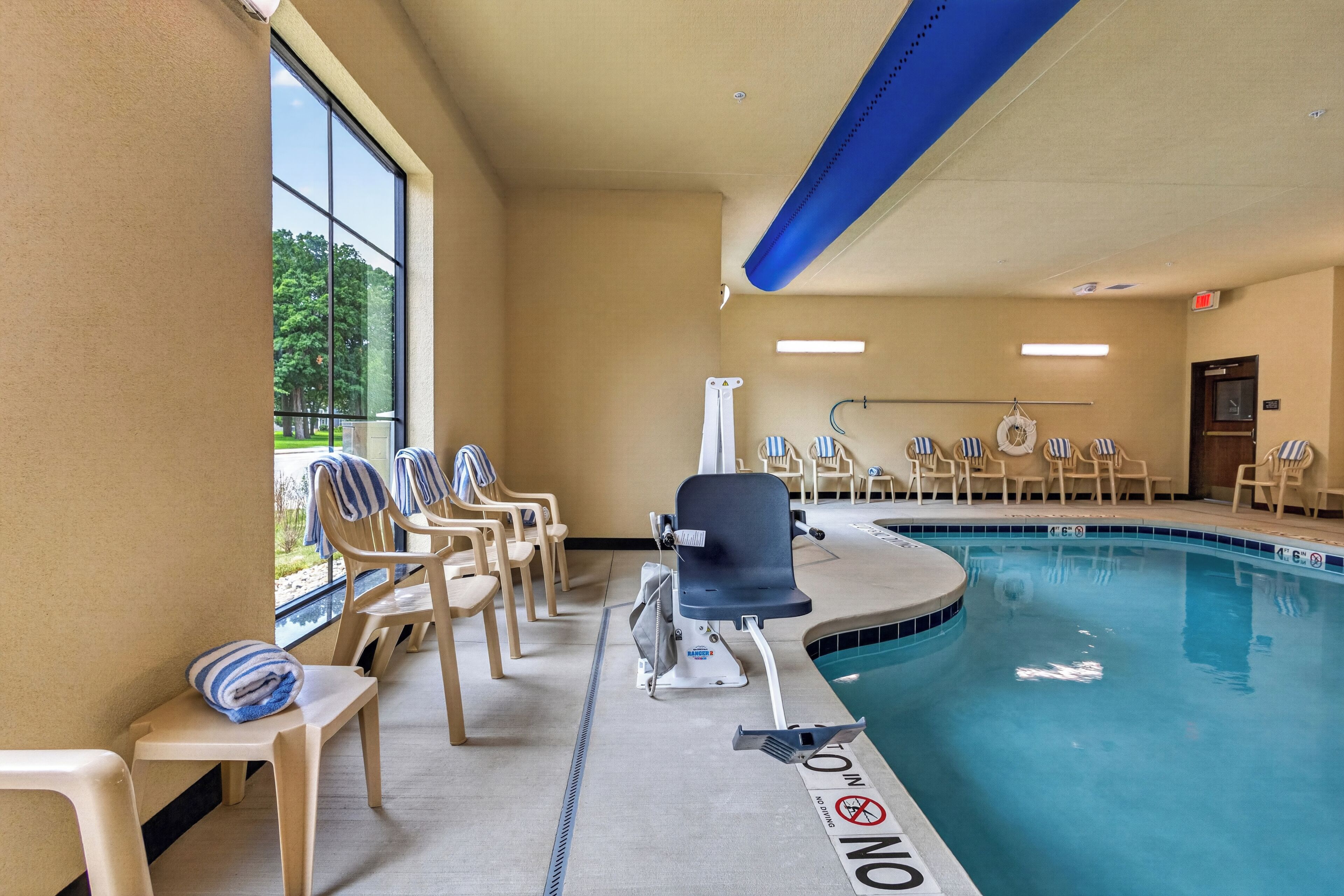 An indoor swimming pool with a lifeguard chair, lounge chairs, and a no diving sign.