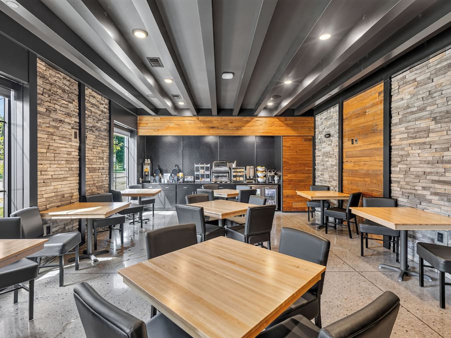 Un interior de restaurante moderno con paredes de ladrillo, mesas de madera y sillas negras.
