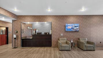 A reception area with a reception desk, a mounted television, and two armchairs.