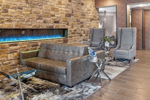 A modern lobby with a stone wall, a leather sofa, a glass coffee table, and a grey armchair.