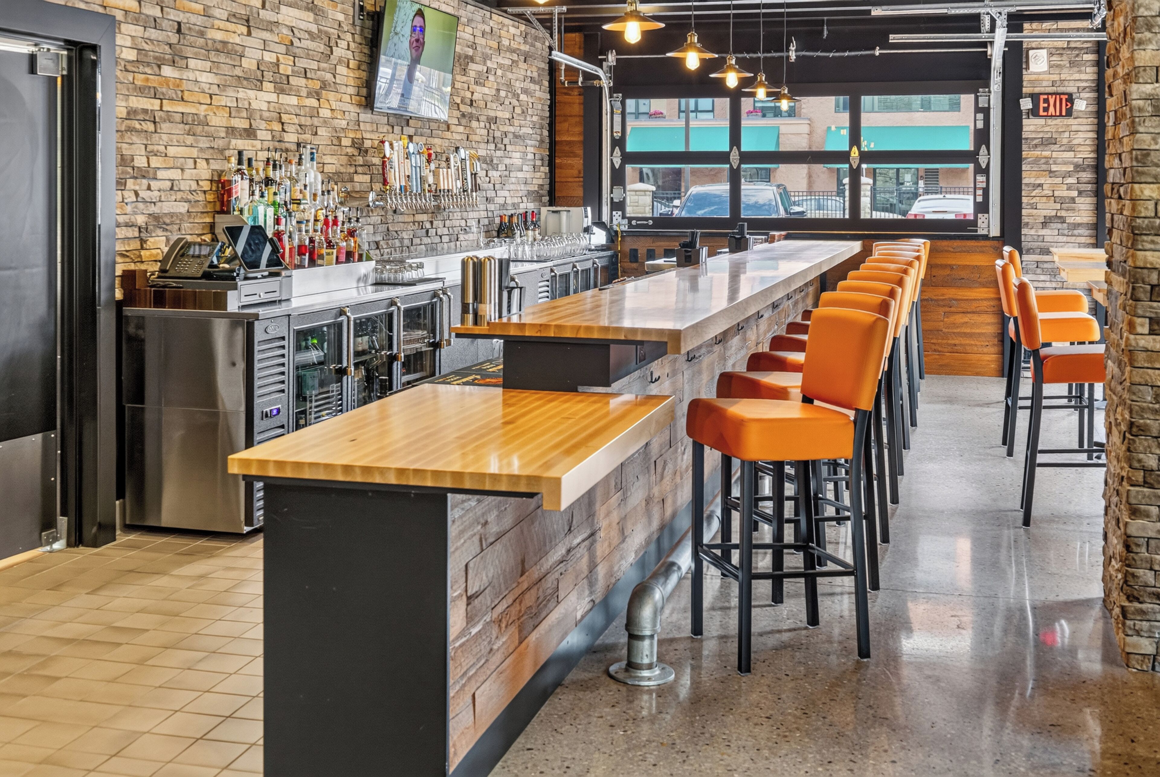 A bar area with a long counter, stools, and a television screen.
