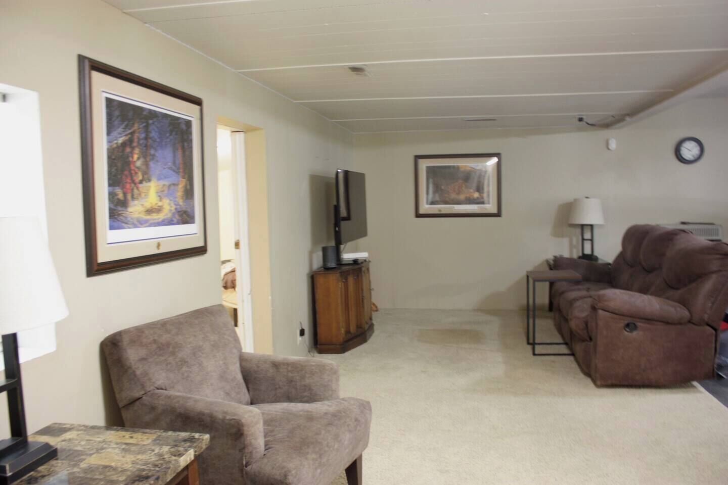 Una sala de estar con un sillón marrón, un sofá, un televisor y cuadros en las paredes.
