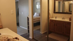 A bathroom with a large mirror, wooden cabinets, and a bed visible through a glass door.