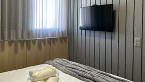 A hotel room with a bed, a TV mounted on the wall, and a window with curtains.